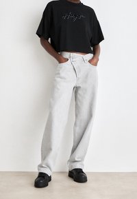 Zkrácená černá trička s vyšitým logem v kombinaci s světlými šedými džínami s vysokým pasem a černými teniskami. Hladká látka a volný střih.