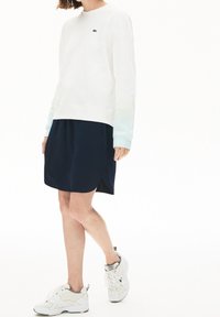 Felpa bianca con polsini a degradé blu, gonna blu navy con orlo curvo e sneakers bianche con dettagli grigi e lacci.