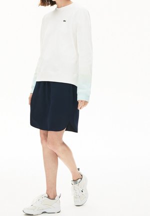 Felpa bianca con polsini a degradé blu, gonna blu navy con orlo curvo e sneakers bianche con dettagli grigi e lacci.