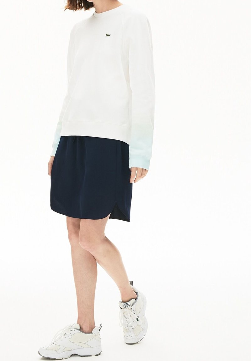 Felpa bianca con polsini a degradé blu, gonna blu navy con orlo curvo e sneakers bianche con dettagli grigi e lacci.