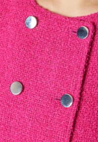 Tissu texturé rose vif avec quatre boutons ronds argentés brillants disposés dans un style croisé près du décolleté.