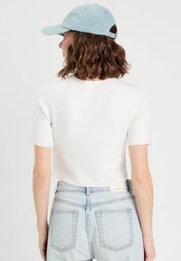 Haut blanc à manches courtes avec un design ajusté, associé à un jean en denim taille haute de couleur bleu clair. La casquette présente une texture en denim.
