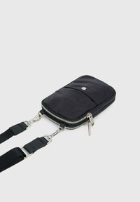 Sac crossbody noir en nylon avec fermeture éclair, poche avant et hardware en métal argenté. Il dispose d'une sangle ajustable et d'une texture lisse.