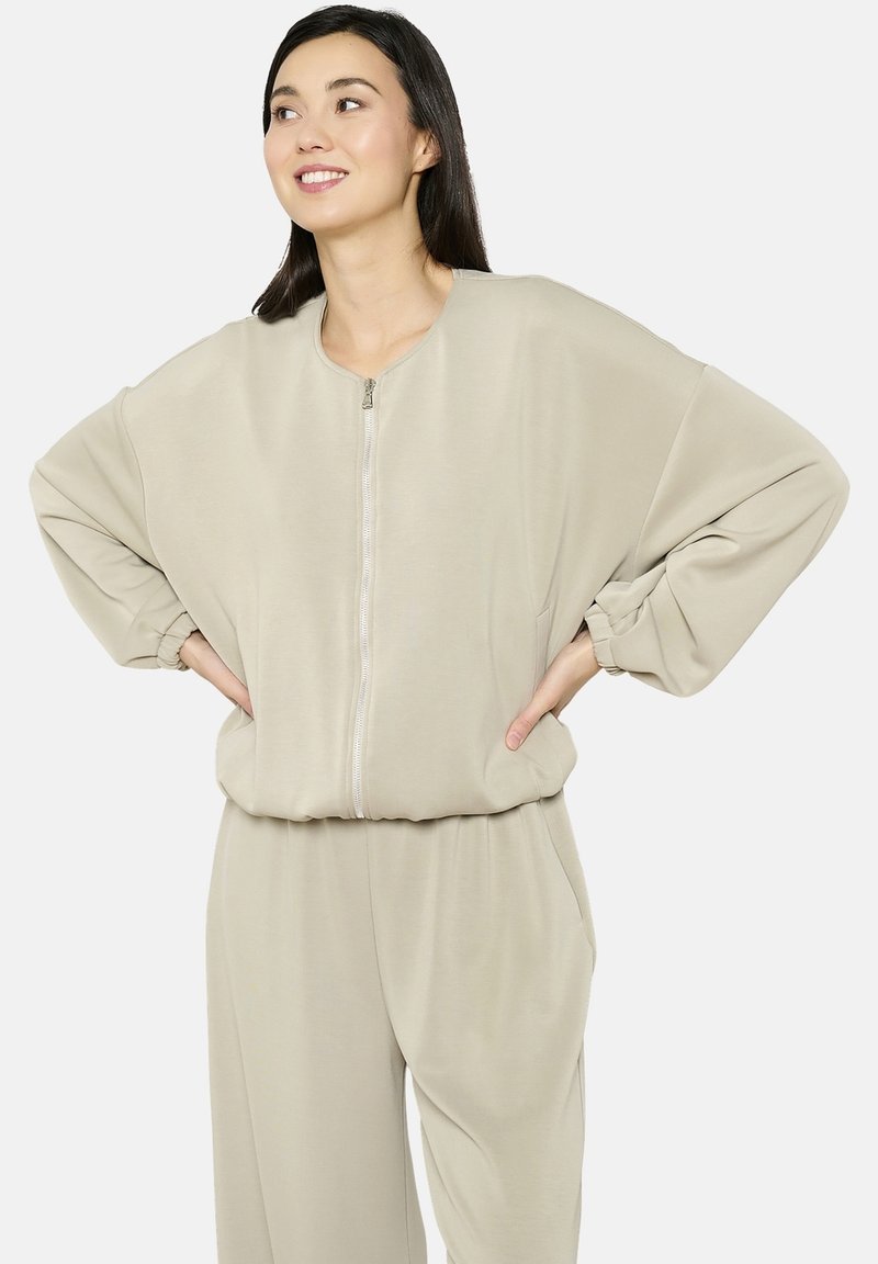 Felpa beige con zip, maniche oversize e scollatura tonda, realizzata in materiale morbido; abbinata a pantaloni coordinati.