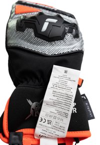 Zwarte en oranje handschoen met een gestructureerde, reflecterende grijze bovenkant, voorzien van een zwart logo en een aangehechte verzorgingslabel. Versterkt ontwerp voor duurzaamheid.