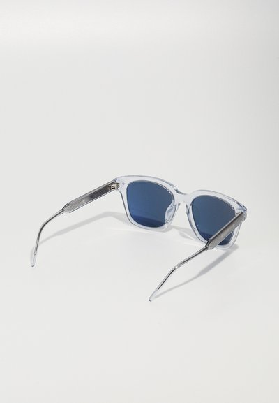 Clear plastic framed sunglasses with dark blue lenses and silver metal arms, featuring textured detailing on the sides.
