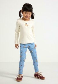 Långärmad krämfärgad skjorta med renbroderi; blå leggings med blommönster och djurtryck; bruna skor med snörning; avslappnad passform.