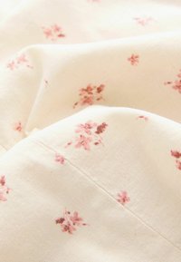 Tissu crème doux avec de petits imprimés floraux roses et bruns dispersés, montrant la texture et de doux plis.