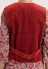 Gilet en velours côtelé rouge avec des raies verticales, comportant une sangle dans le dos et deux boutons. Assorti avec un tissu à motif floral sur les manches.
