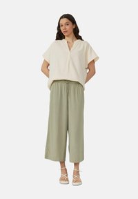 Haut en crème léger avec des manches courtes et larges, et un col à cran, associé à un pantalon large olive. Des sandales légères complètent la tenue.