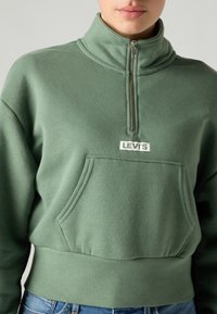 Sweat-shirt polaire vert à col montant, zip quart de fermeture et poche avant. Logo blanc "LEVI'S" sur la poitrine.