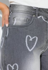 Grå denimjeans med hvide hjerteprint, fem-lomme-design, sølvfarvet hardware og en talje i midjehøjde, med en blød tekstur og en falmet finish.