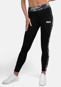 Schwarze Leggings mit einem camouflagemusterten Bund und seitlichen Einsätzen, auf der Vorderseite mit einem weißen Lonsdale-Logo. Glattes, dehnbares Material.