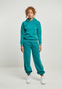 Tūbēra krāsas kokvilnas kapuci ar auklu un ribotām piedurkn�ēm, saskaņotas ar atbilstošām sašaurinātām sporta biksēm ar elastīgu oderi potīs. Baltas sporta apavi.