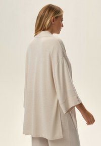 Jasnobeżowy, oversize sweter z ribbowanym kołnierzem i szerokimi rękawami, wykonany z miękkiej, teksturowanej tkaniny z bocznymi rozcięciami dla wygody.