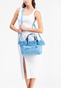 Borsa intrecciata blu con bordo in tessuto frangiato, testo ricamato "Playa del Mar", doppi manici e tracolla regolabile. La texture è morbida e leggera.