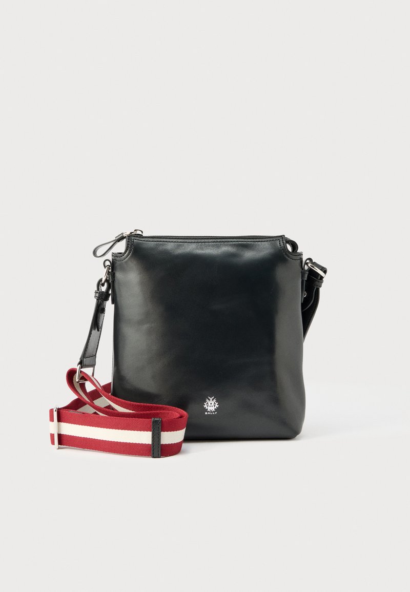 Μαύρη δερμάτινη τσάντα crossbody με ρυθμιζόμενο λουρί ώμου κόκκινου και λευκού χρώματος με ρίγες και μικρό ασημί λογότυπο στο κέντρο της πρόσοψης.