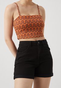 Top corto de tirantes con un patrón ondulado en naranja y marrón, combinado con unos pantalones cortos de mezclilla negros de cintura alta con dobladillos enrollados y bolsillos frontales.
