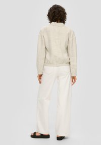 Beige linen jacket with elastic waistband, paired with white wide-leg trousers and black slide sandals. Visible seams and relaxed fit.