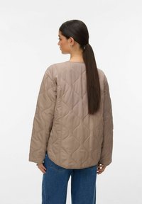 Bež bunda s odebeljenim vzorcem, okrogel izrez, dolgi rokavi in teksturiranim vzorcem. Oblečena z modrimi jeans hlačami, ki prikazujejo sproščen kroj.