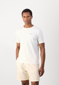 Witte katoen t-shirt met korte mouwen en een ronde hals, voorzien van een klein zwart logo op de borst, gecombineerd met lichtbeige shorts.