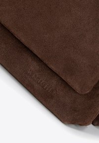 Brązowy zamsz o miękkiej teksturze, charakteryzujący się gładkim kształtem i subtelnym wytłoczonym logo. Czyste krawędzie i jednolity kolor.