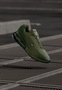 Nike running shoe in dark green mesh with a textured finish, featuring a black sole and subtle branding on the side, suspended above a grid.