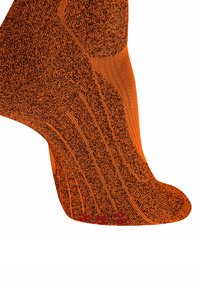 Calzino arancione e nero a motivo su un piede, mostrando in dettaglio la trama del tessuto lavorato a maglia e le aree rinforzate sul tallone e sulla suola.