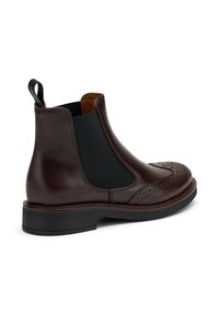 Botas Chelsea de cuero marrón con paneles laterales elásticos, detalles de brogue y suela de goma negra. Incluyen una pestaña en la parte posterior para facilitar el calzado.