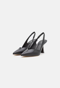 Tacones slingback de cuero negro con punta afilada y detalle recortado, que presentan un tacón triangular y una textura suave.