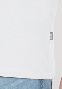 Witte katoenen T-shirt met een rechte snit; fijne textuur. Heeft een grijze label met "JAKO" aan de zijkant onderaan.
