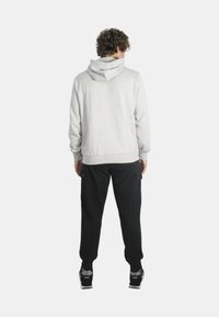 Felpa grigia con tasca a marsupio, polsini e orlo a coste, abbinata a pantaloni neri con tasche laterali e scarpe da ginnastica con suola bianca.