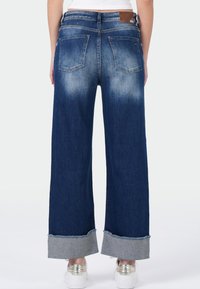 Wijdvallende blauwe jeans met een vervaagd effect, twee achterzakken en een omgeslagen zoom die een contrasterende binnenlaag van denim onthult.