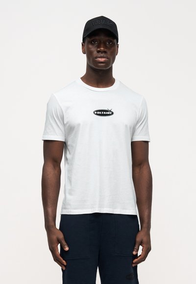 Bílé bavlněné tričko s kulatým výstřihem, na hrudi černé logo, doplněné tmavě modrými kraťasy a černou kšiltovkou.