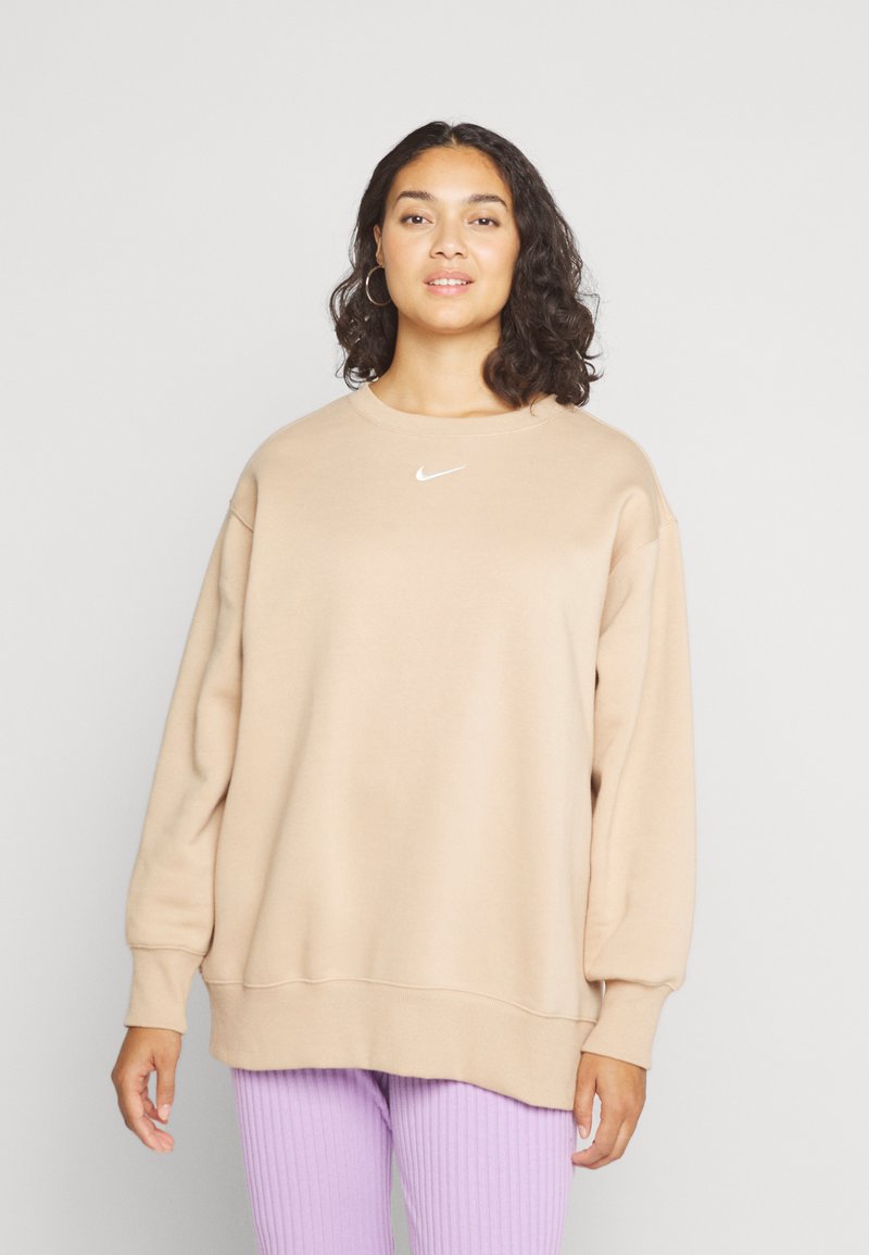 Sweatshirt beige avec un col rond, des épaules tombantes et des poignets élastiques. Présente un petit logo Nike blanc sur la poitrine. Texture douce.