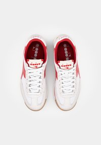 White athletic shoes with red accents, textured leather and mesh materials, flat laces, and a gum rubber sole. Diadora logo on the tongue.