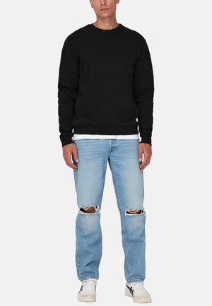 Zwarte crewneck sweatshirts, lichtblauwe distressed jeans met gescheurde knieën, witte ondershirt zichtbaar, witte sneakers met zwarte accenten.