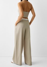 Top corto ajustado beige con corte recto, combinado con pantalones de pierna ancha. Los pantalones tienen bolsillos laterales y un acabado de tejido texturizado.