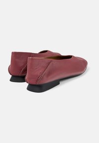 Zapatos planos de cuero burdeos con punta redonda, costuras mínimas y un tacón bajo negro. Textura suave y diseño sencillo.