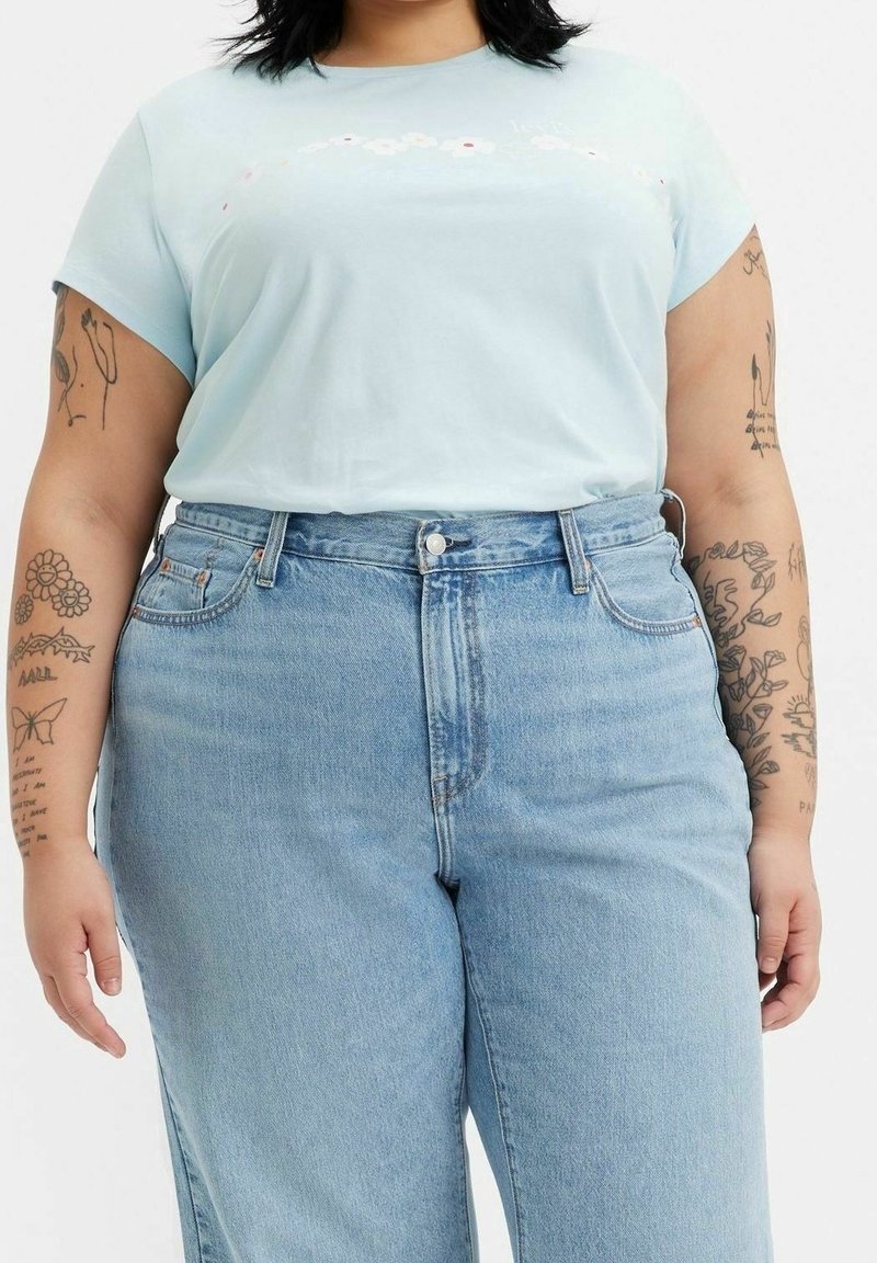 Camiseta de algodón azul claro con mangas cortas, que presenta bordados florales. Combinada con unos jeans de mezclilla azul claro de cintura alta y desgastados.