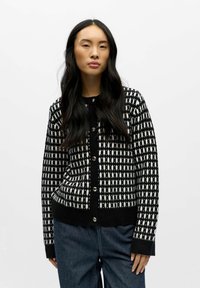 Melnā un baltā rakstu džemperis ar ribotu apakšmalu un piedurknēm, ar spīdīgām pogām priekšpusē. Strukturēta, adīta auduma.