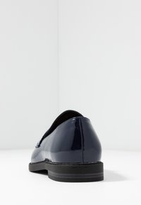 Marinblå lackskinnsloafer med en slät, glänsande yta och en låg, svart klack. Rundad tå och minimalistisk design, lämplig för avslappnad användning.