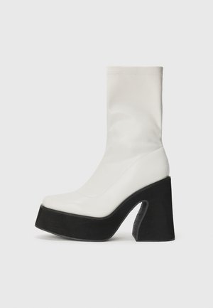 Botine albe până la gleznă, cu un toc înalt negru, din material sintetic neted, cu o formă structurată și vârf alungit. Prezintă o decupare laterală.