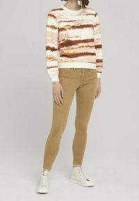 Suéter con un patrón ondulado en rosa y marrón, base crema; combinado con jeans ajustados en color beige y zapatillas altas blancas. Outfit casual.