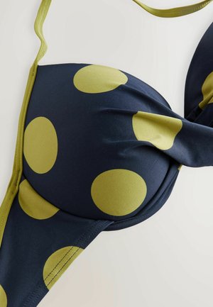 Námořnická modrá bikiny horní část s velkými olivově zelenými puntíky. Má hladkou tkaninu, polstrovaný design a nastavitelné ramínka.