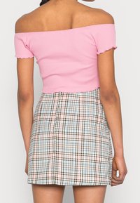 Růžový žebrovaný crop top bez ramínek s volánovými okraji, spárovaný s kostkovanou minisukní s modro-hnědo-růžovými vzory.