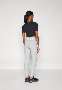 Svart kortermet crop topp og lysegrå tights med høy livlinje, kombinert med svarte treningssko, alt laget av glatte stoffer.