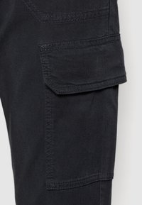 Svarta cargobyxor i tyg med en sidficka, med robust sömnad och en mjuk textur. Designen betonar praktisk användning och hållbarhet.