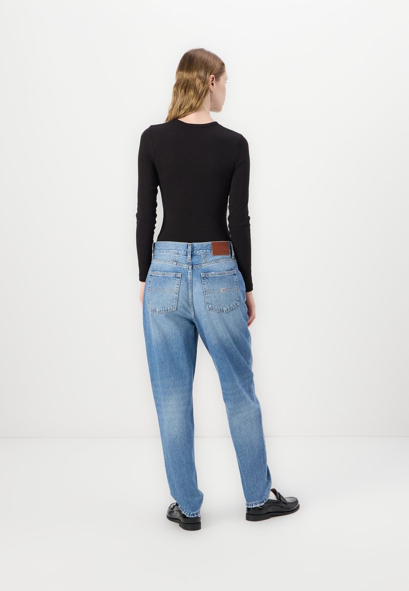 Jean en denim bleu clair à coupe décontractée avec une étiquette en cuir au dos, associé à un haut noir à manches longues. Texture lisse, design décontracté.