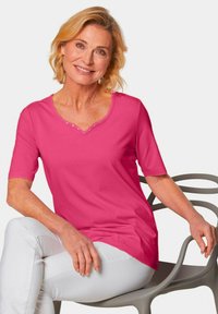 Rosa Kurzarm-T-Shirt mit V-Ausschnitt und dekorativen Knöpfen. Glatte Stoffoberfläche und lockere Passform, kombiniert mit weißen Hosen.
